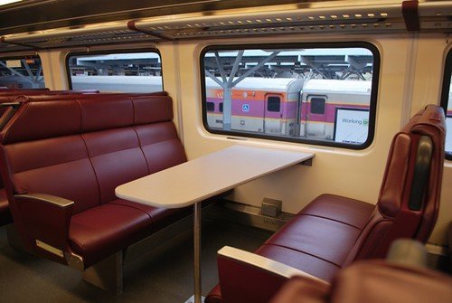 窓際に赤い座席が向かい合う列車の車内の写真
