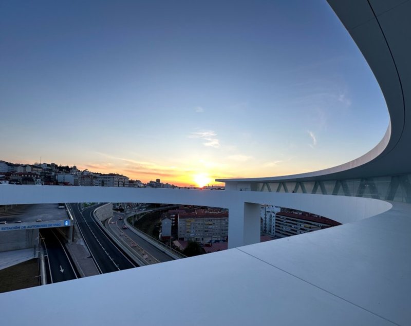 夕焼けの空の下、弧を描く高架の通路と遠くの街並みが見える写真