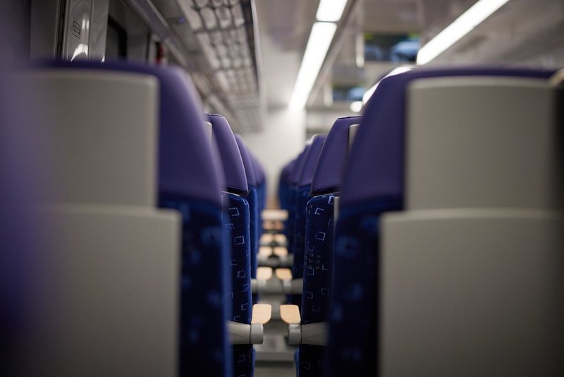 人のいない列車の車内に、青い座席がまっすぐ並んでいる写真
